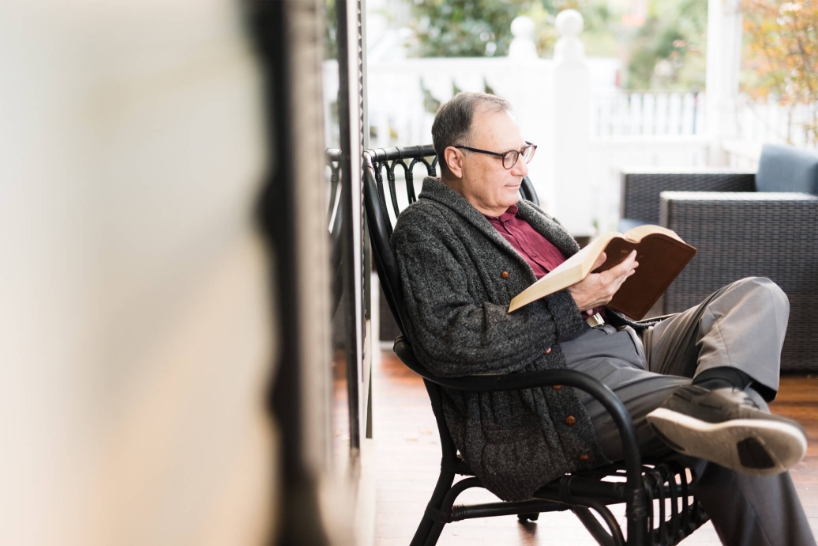 Man reading his Bible in a chair on a porch.